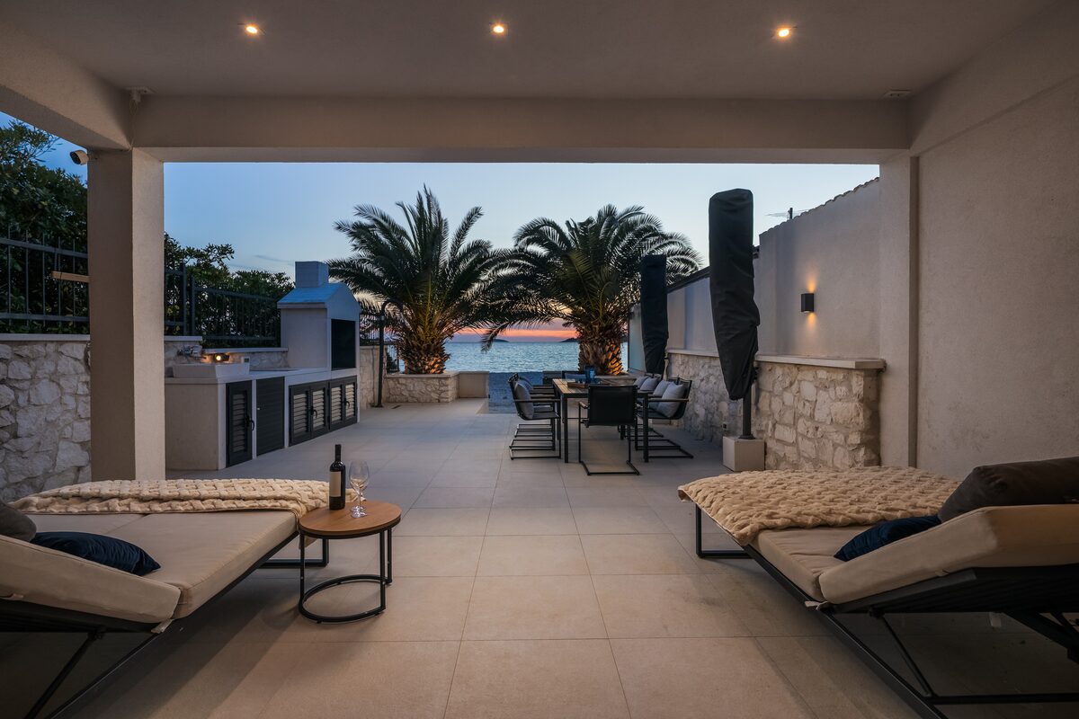 The Beachhouse Rogoznica terrace at twilight with lights coming on across the bay
