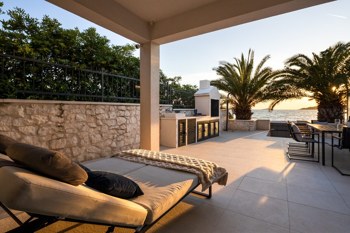 The Beachhouse terrace with stone paving, dining table for eight, twin parasols and palms framing the sea